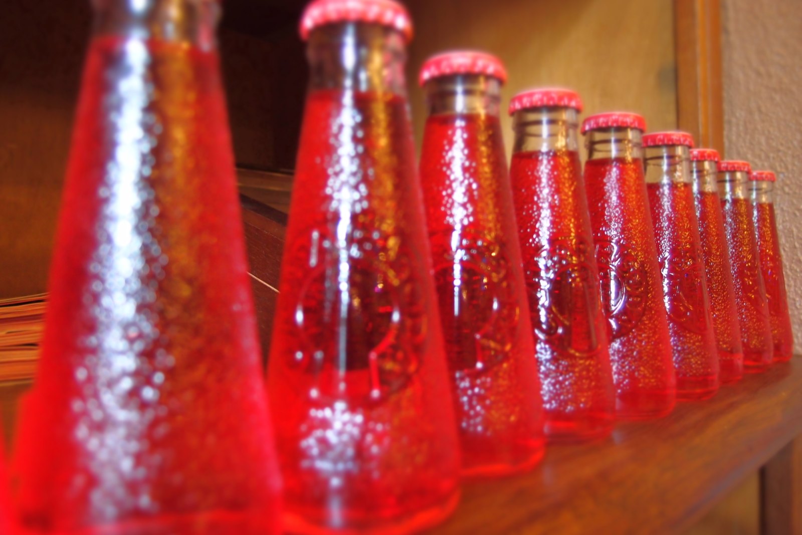 Uma fileira de garrafinhas vermelhas de Campari Soda numa prateleira de madeira, com o vidro texturizado brilhando.